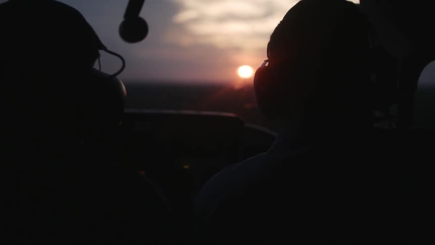 Two people in a dark plane traveling as the sun sets