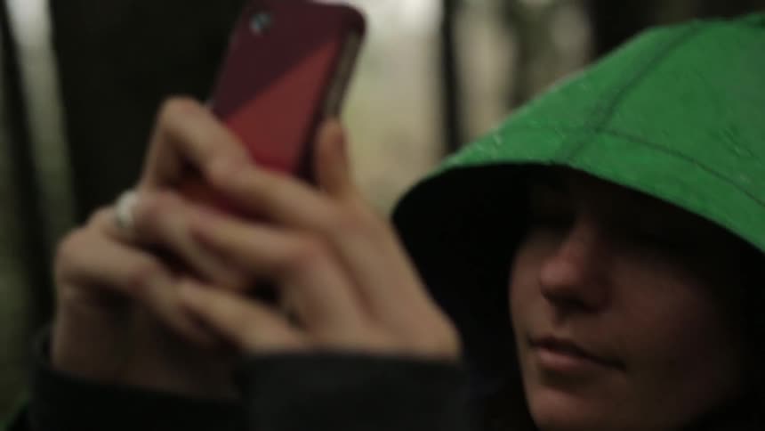 Woman standing in forest using her phone in the rain