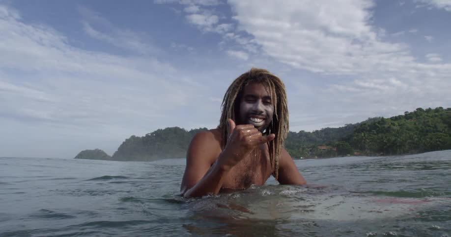 Black man holding a surfboard swims in the sea