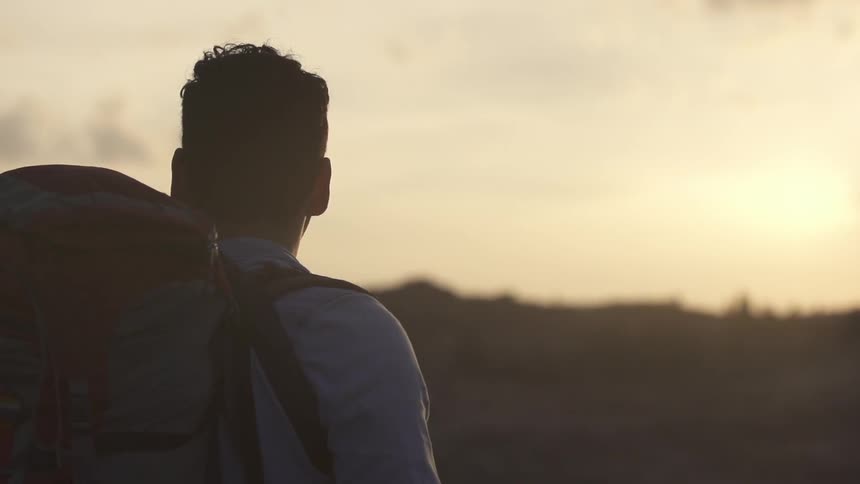 A man with a backpack looks out towards the horizon