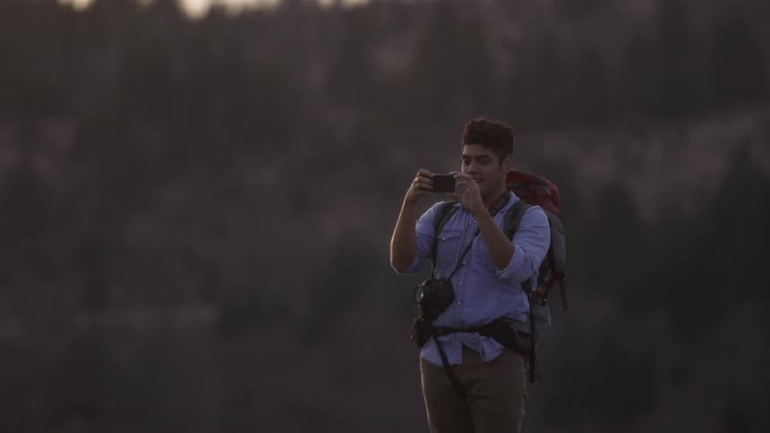 A young man wearing a large backpack and photographing something