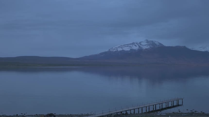 A calm lake on a cloudy day with a snow-capped mountain in the background