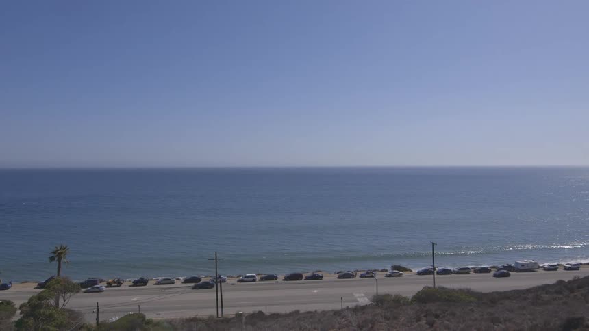 Cars drive past a beach on a sunny day