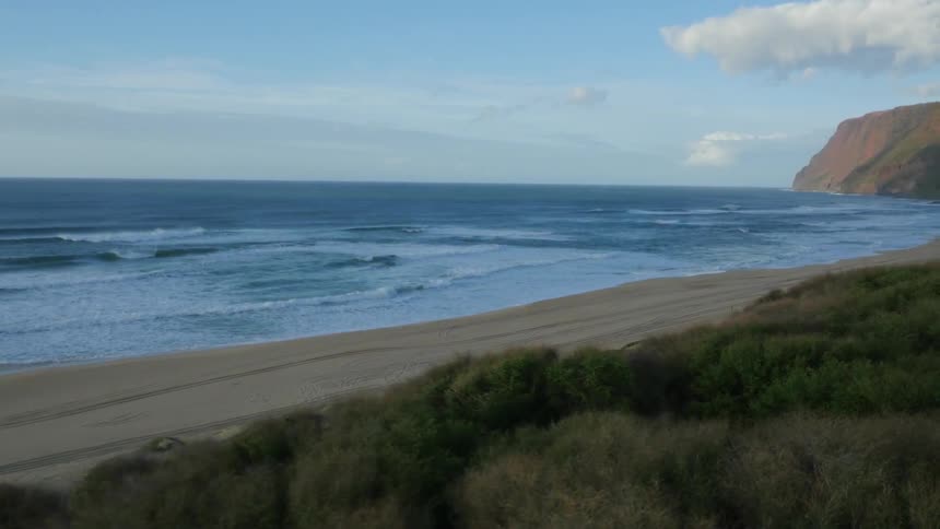 An empty beach with cliffs in the background and rolling waves