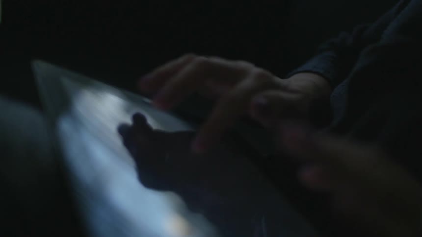 Man sitting in a dark room using a tablet