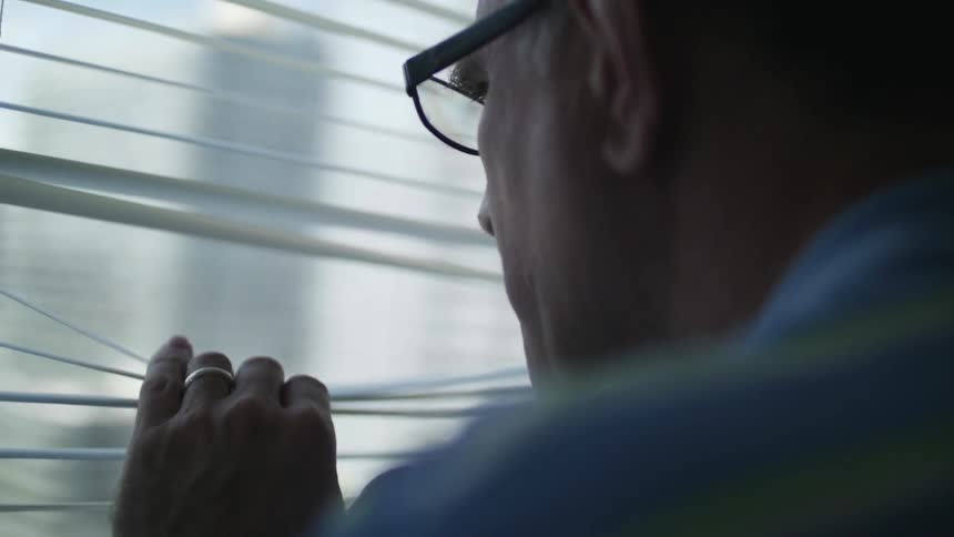 Man wearing glasses peaks out a window