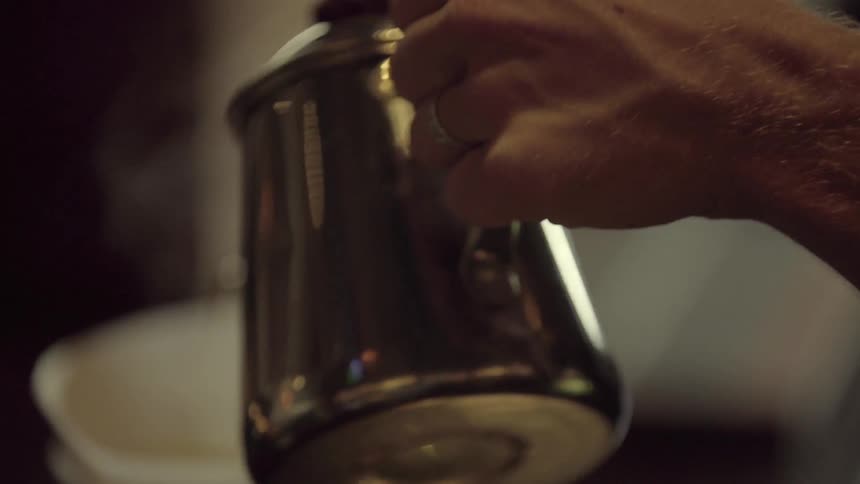 A man pours a hot and steaming beverage from a kettle