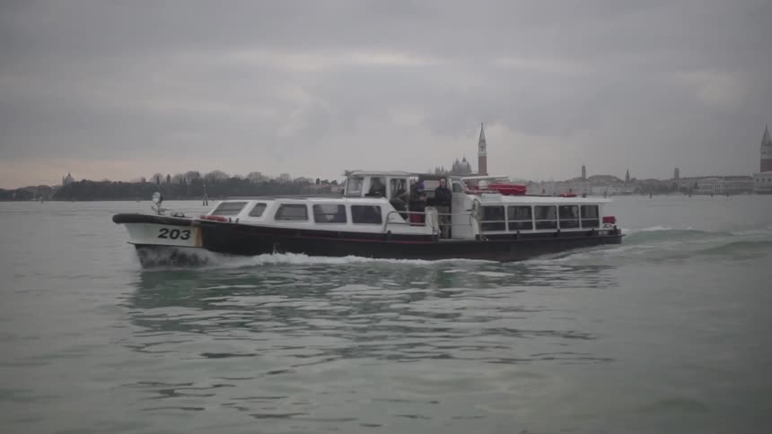 A boat travelling over water with buildings and heavy clouds in the background