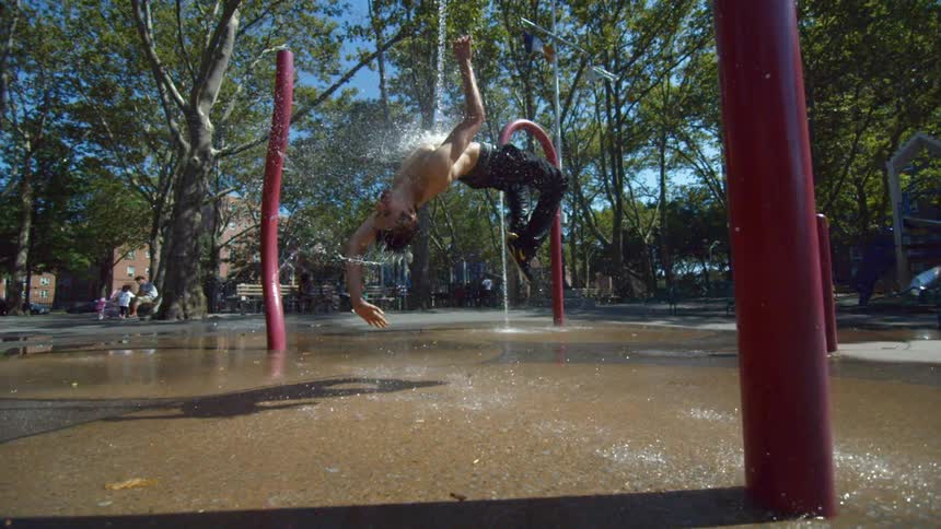 Man doing a backflip as water pours on him in a park