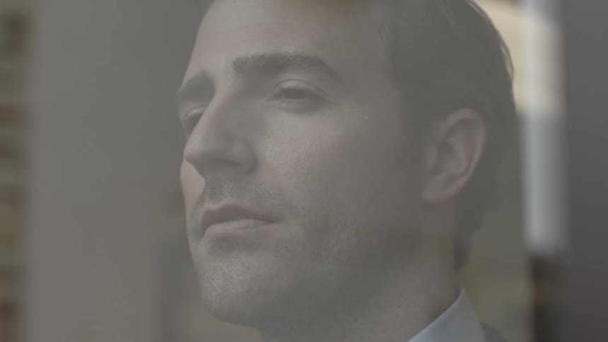 A man standing behind a window and looking out