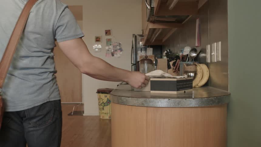 A man putting on a brown messenger bag then walking towards a door