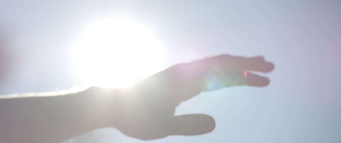 An outstretched hand turning into a fist and twisting around as the sun glares behind it