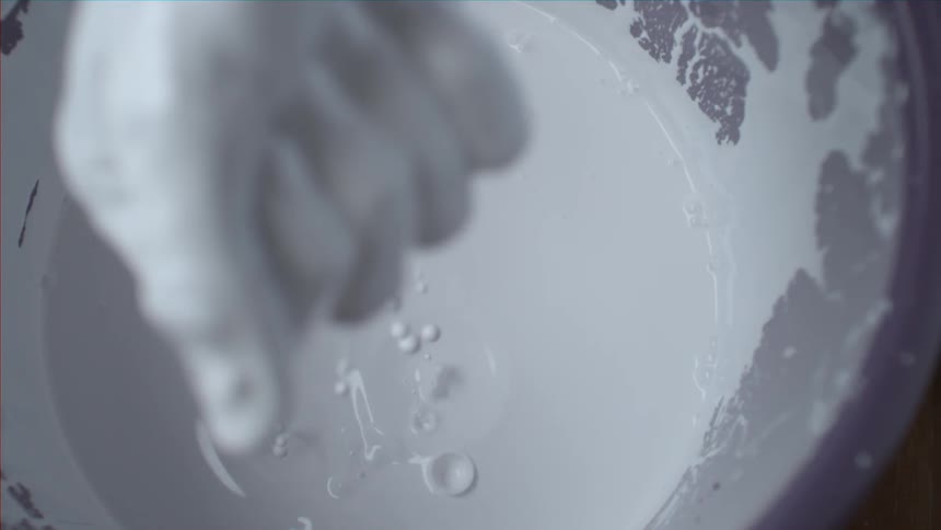 Someone pulling their hand out of a bucket of paint while paint drips off their hand and back into the bucket