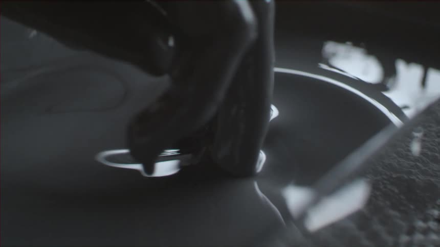 A hand stirs gray liquid in a container