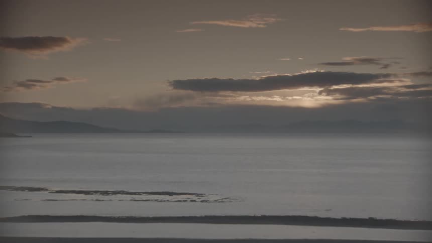 Time lapse of clouds floating over ocean water while the sun sets