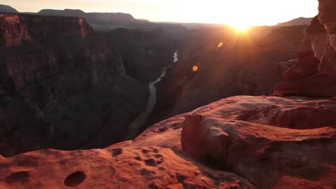 A view of a river running through a canyon as the sun glares in the horizon