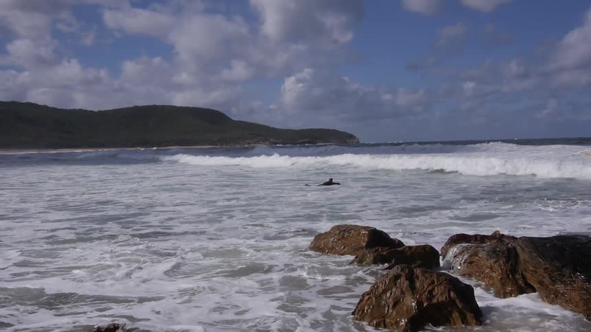 A man is attempting to surf a rocky beach