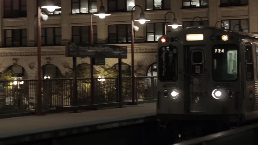 A train coming down the tracks near a large building at night