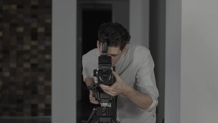 A man using a camera on a tripod and looking through the lens