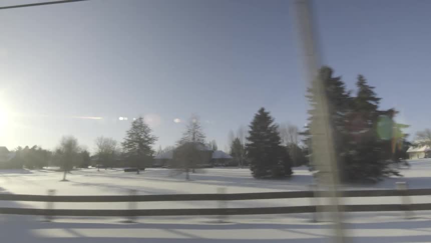 Driving along a road passing snow-covered fields and houses