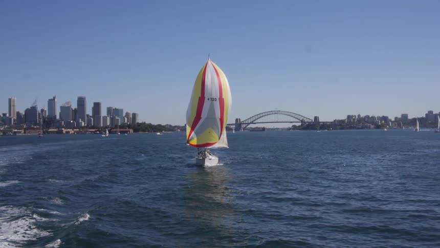 A sailboat slowly sails alongside a harbor