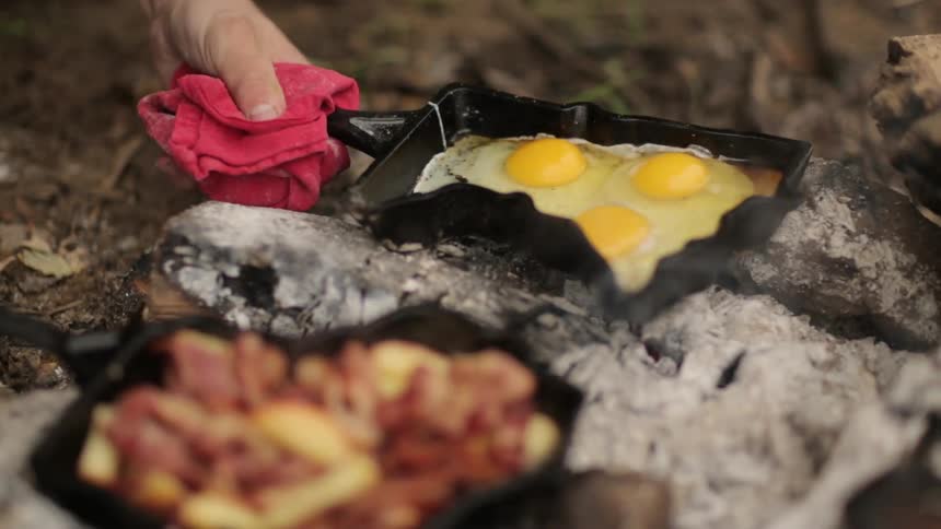 Eggs are poured into a skillet on an outdoor fire