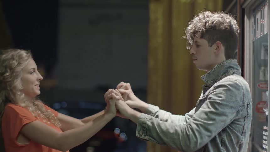 A woman and a man holding hands and talking outside a building at night