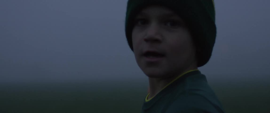 A boy wearing a striped cap standing outside and looking around at night time