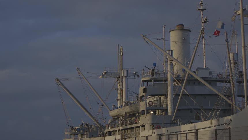 A very large ship with flags that are waving in front of a dark and cloudy sky