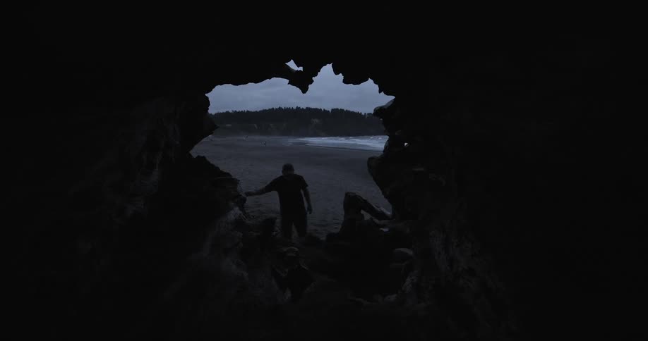 A man walking into a cave on a beach