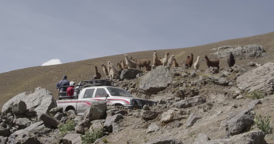 A truck with passengers in the truck bed drive up a rocky hill