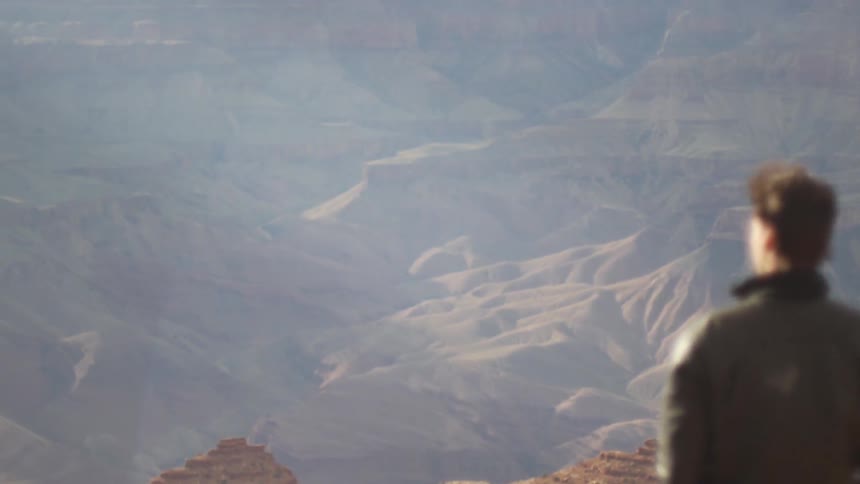 A man standing on top of a mountain looking out at a canyon