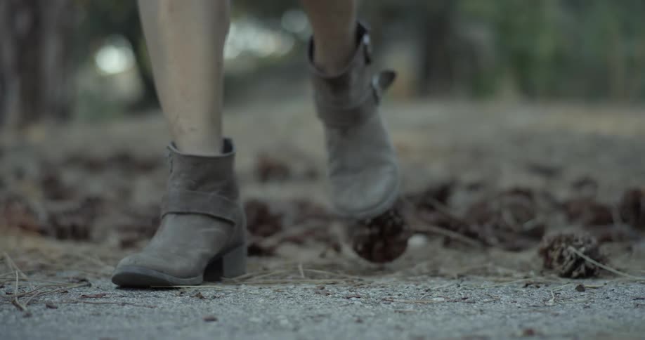 A woman wearing boots walks over pinecones
