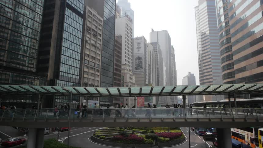 People walking in a covered elevated walkway in a large city