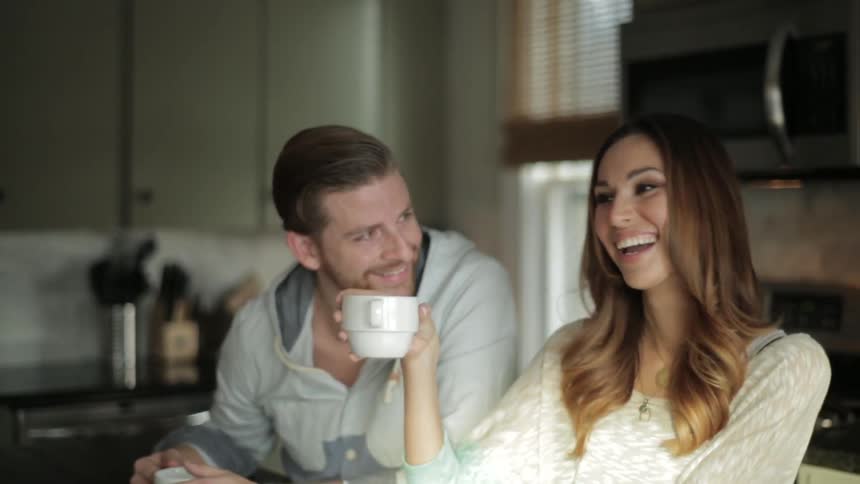 A man and woman laughing over coffee in their kitchen