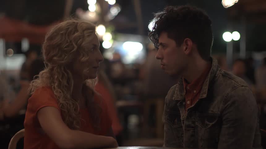 A young couple is heavily engaged in conversation while sitting in a well-lit park at night