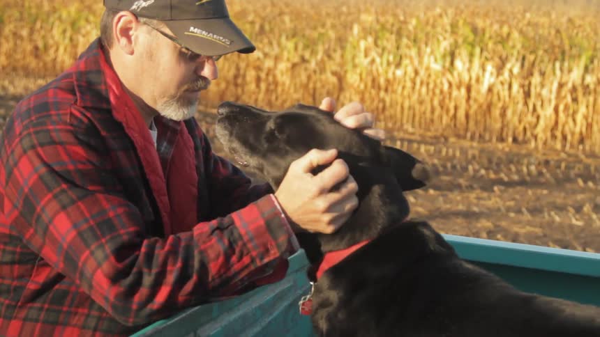 A man pets a black dog that is in the back of a truck