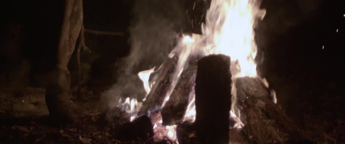 A person kicks the coals in a campfire