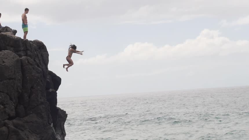 Girl jumps off a rocky cliff into the ocean water