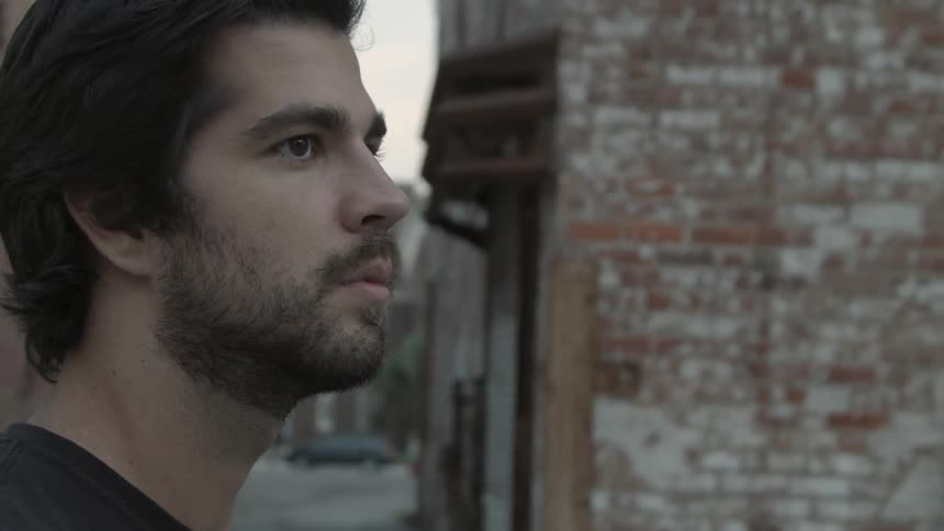 A bearded man is surrounded by brick buildings