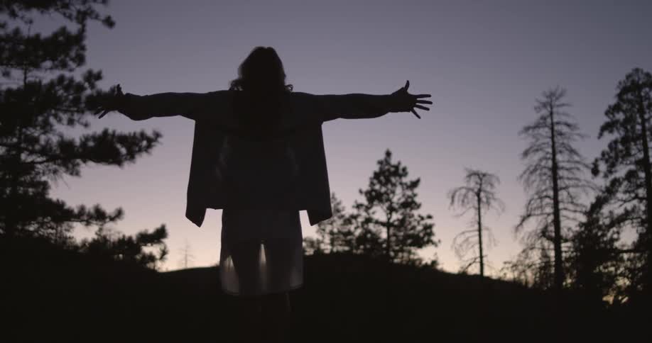Person standing outside in the dusk, outstretching their arms