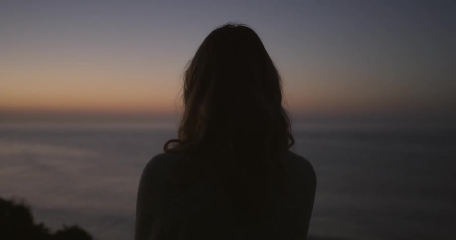 A woman gazes at the ocean at sunset