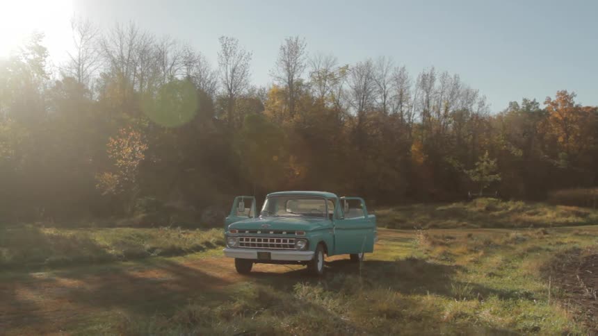 A vintage blue car parked in a grass field at dawn