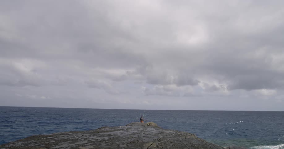 Person standing out on a large rock next to the ocean
