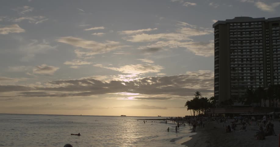 Beachgoers wade into the ocean while the sun sets