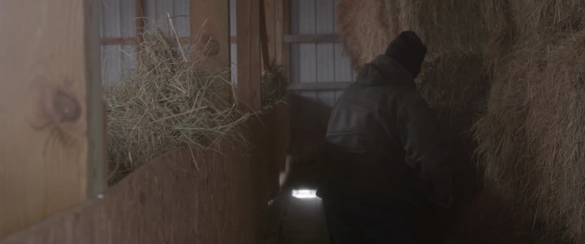 A man shovels hay in a barn