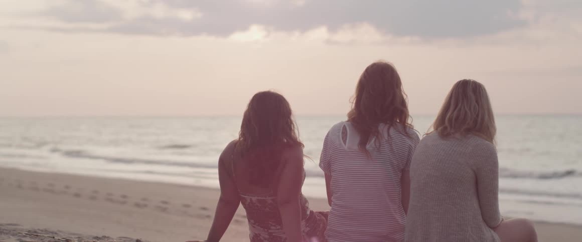 Three women sit on the beach at sunset