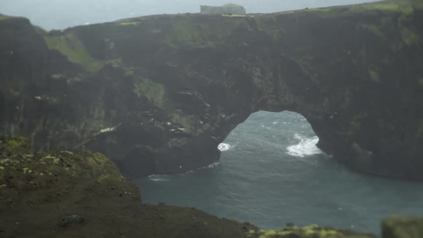 Sea water crashing into a cliff and rushing through a hole in the bottom of the cliff
