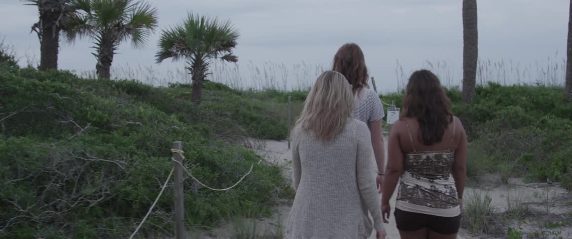 Three women walk along a sandy path