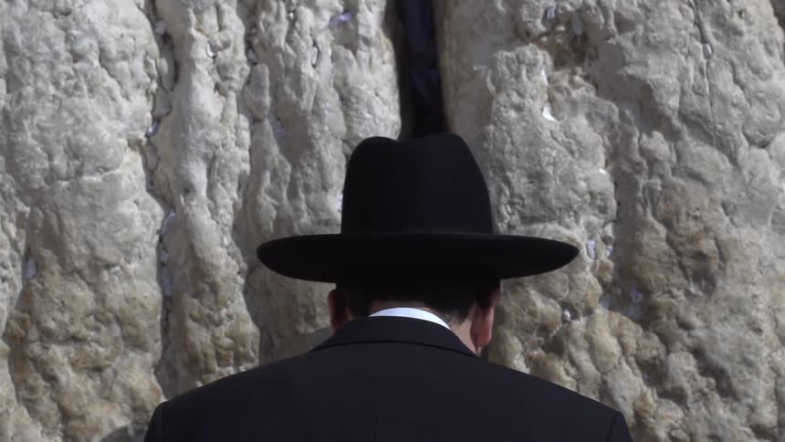 A man in a suit bowing next to a wall of rock
